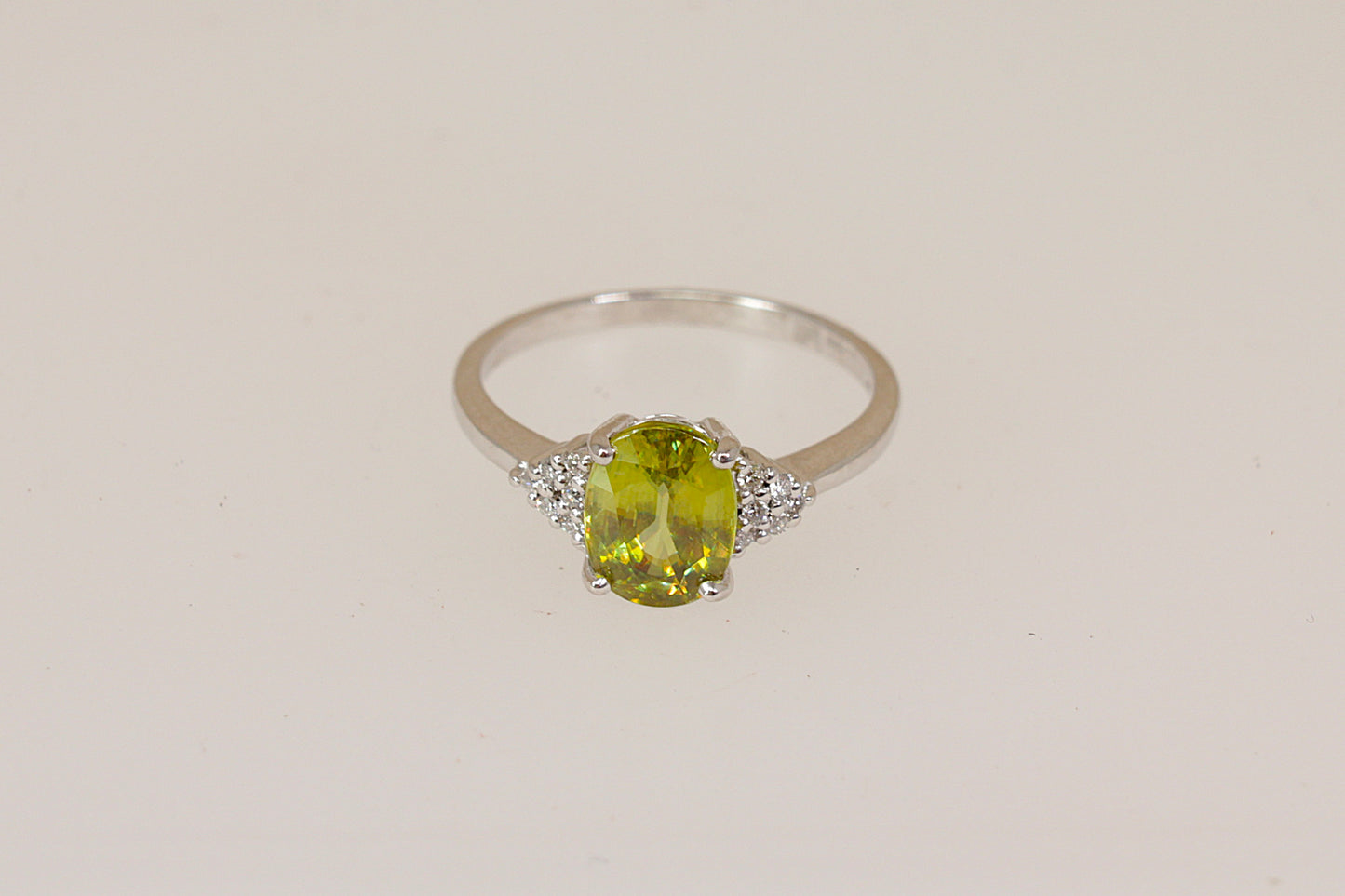 18ct white gold ring with a vibrant green Peridot gemstone with diamond accents on a beige background