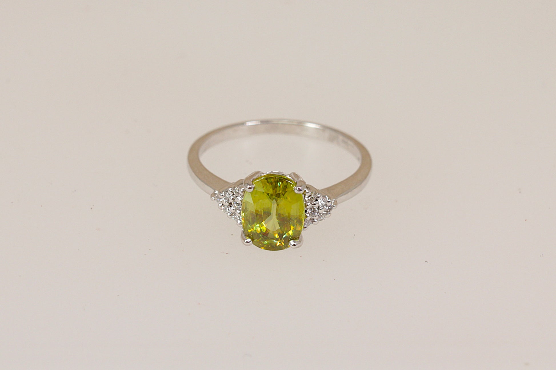 18ct white gold ring with a vibrant green Peridot gemstone with diamond accents on a beige background