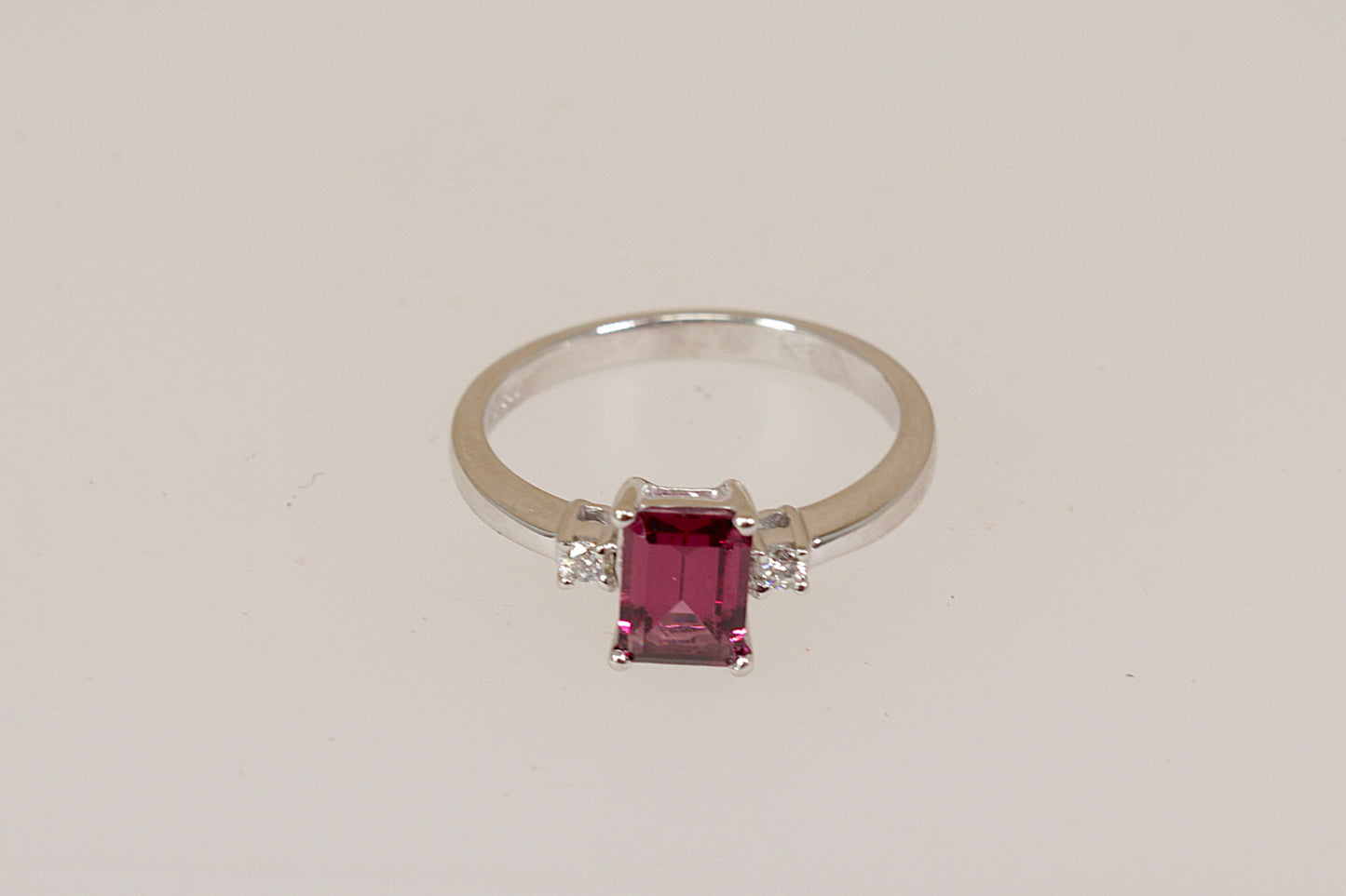 18ct white gold ring with a red rhodolite and diamond gemstones on a light beige background