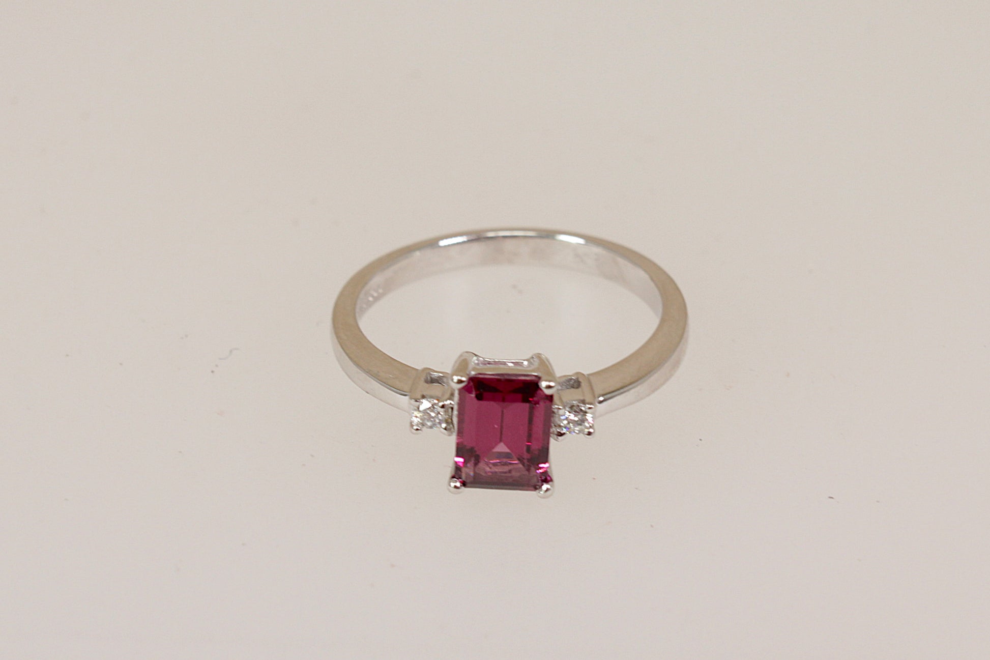 18ct white gold ring with a red rhodolite and diamond gemstones on a light beige background