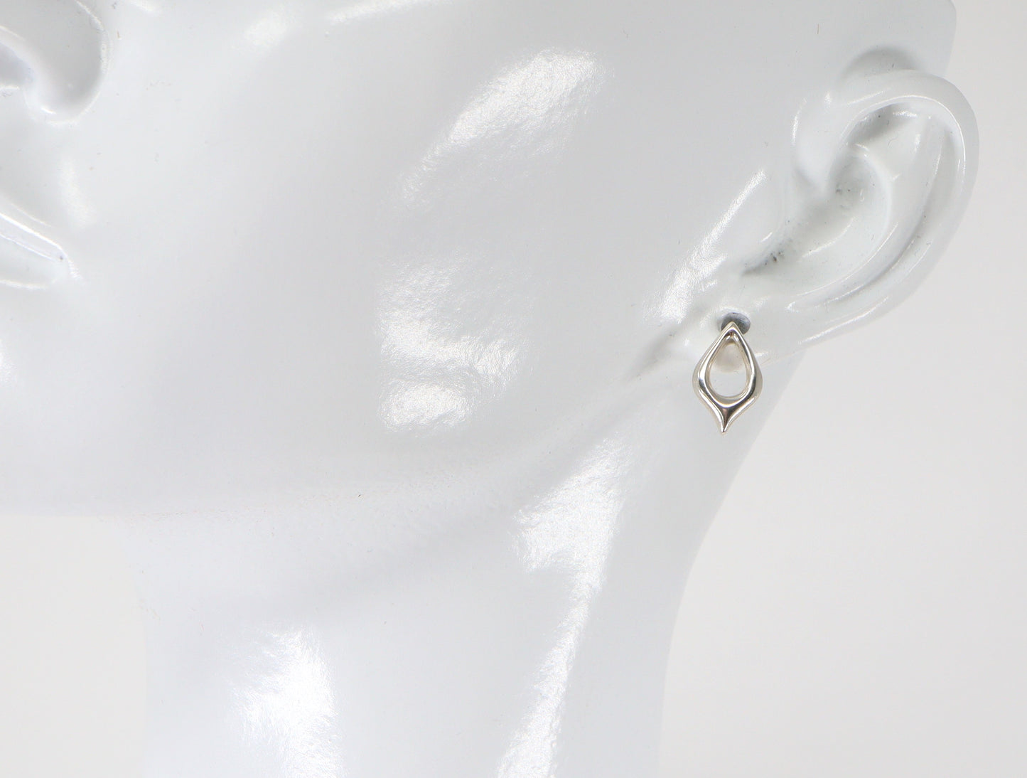 A pair of silver stud earrings in the shape of a petal, displayed on a mannequin ear.