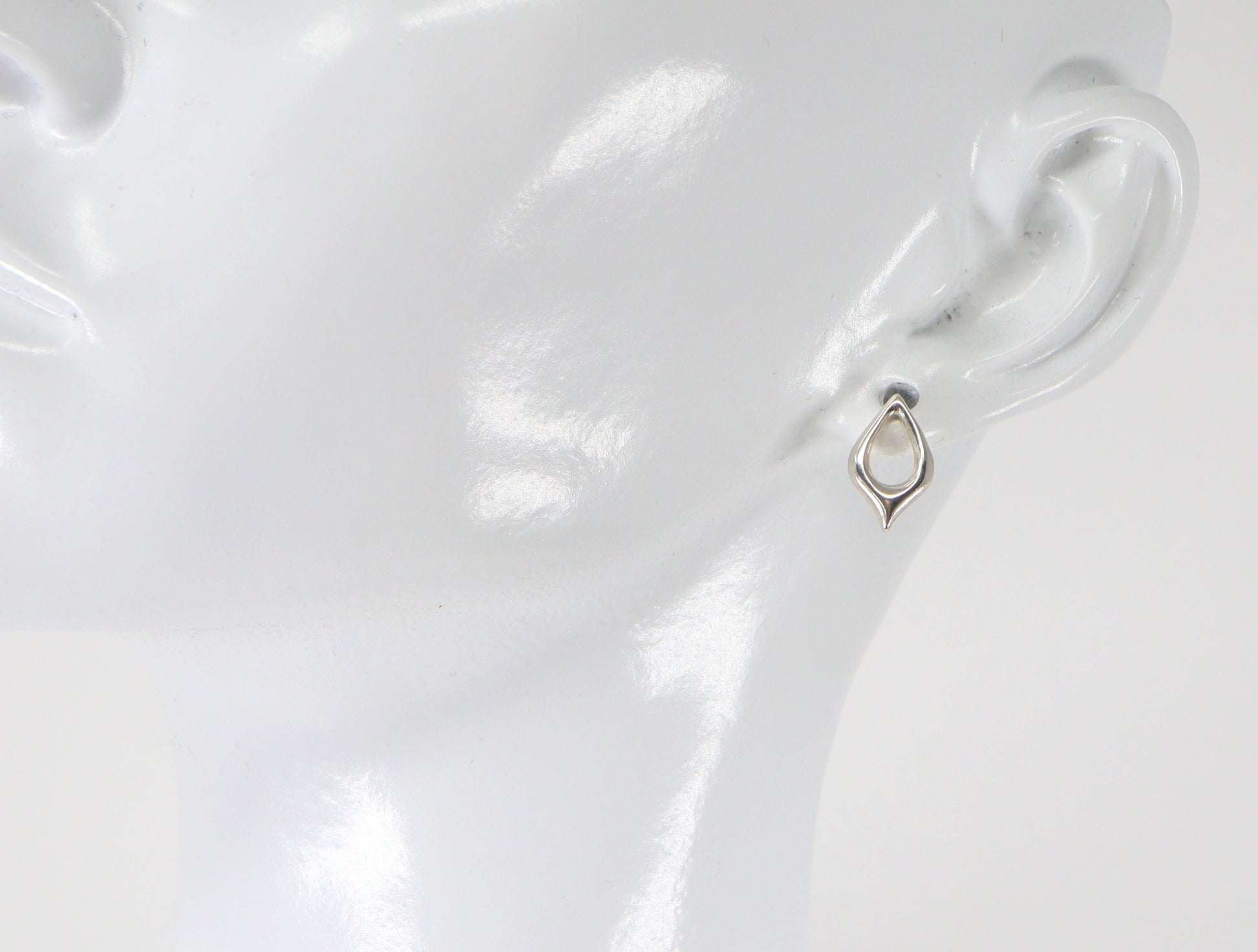 A pair of silver stud earrings in the shape of a petal, displayed on a mannequin ear.