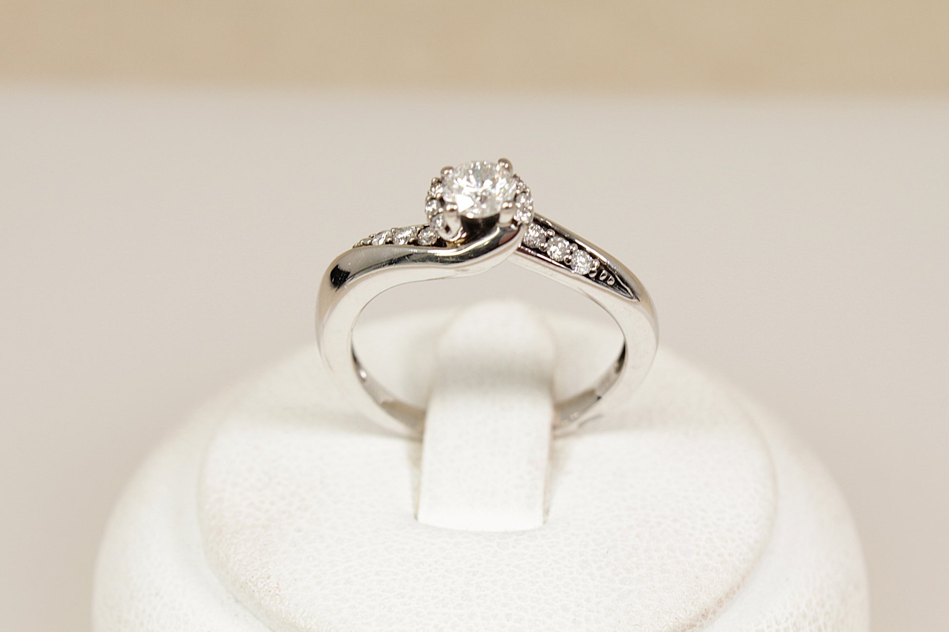 White gold diamond solitaire ring with  diamonds on the shoulders on a white cushion