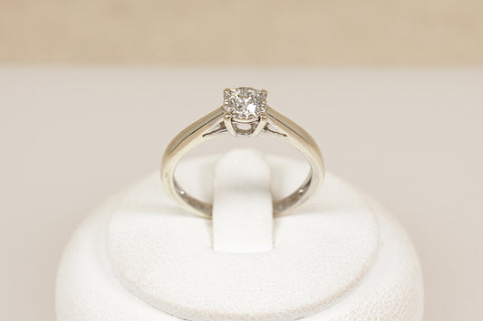 Diamond solitaire ring on a white stand with a beige background