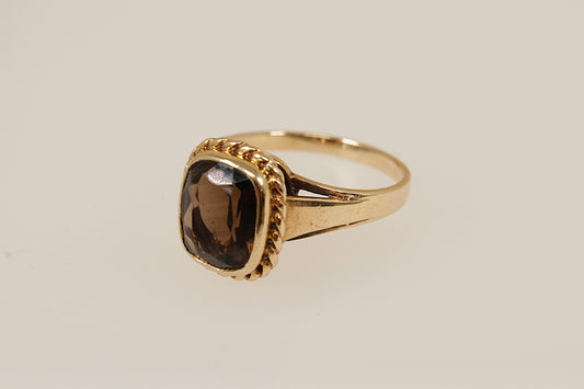 Gold ring with a smoky gemstone on a beige background