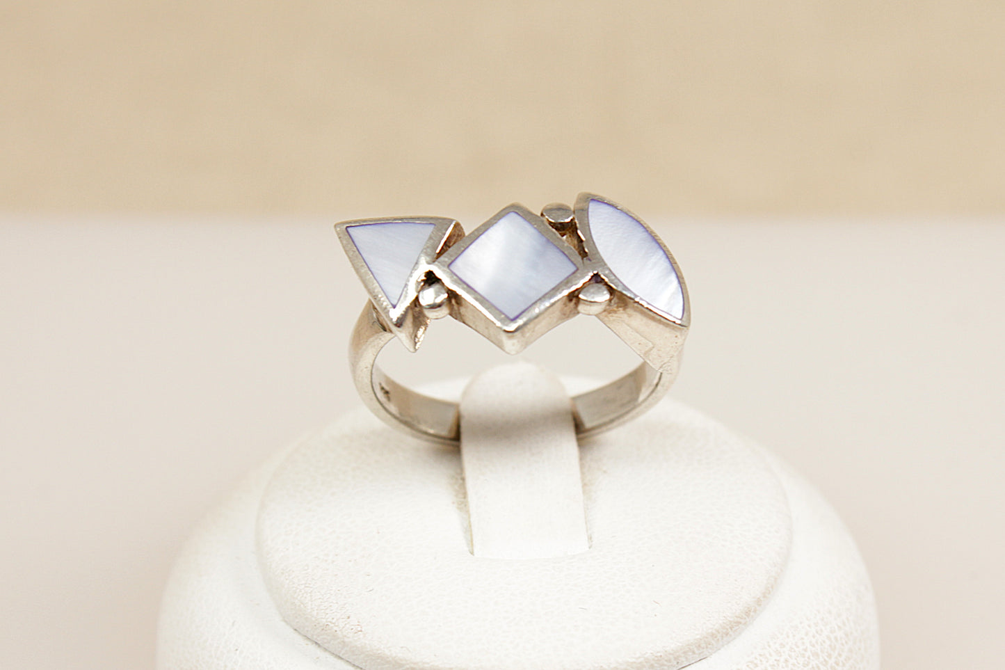 Silver mother of pearl ring with three triangular mop gemstones on a beige background