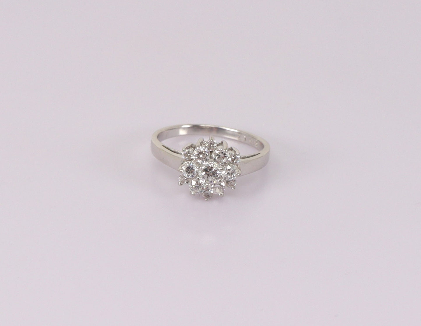 A silver cluster ring with cubic zirconia stones arranged in a daisy pattern, displayed against a white background.