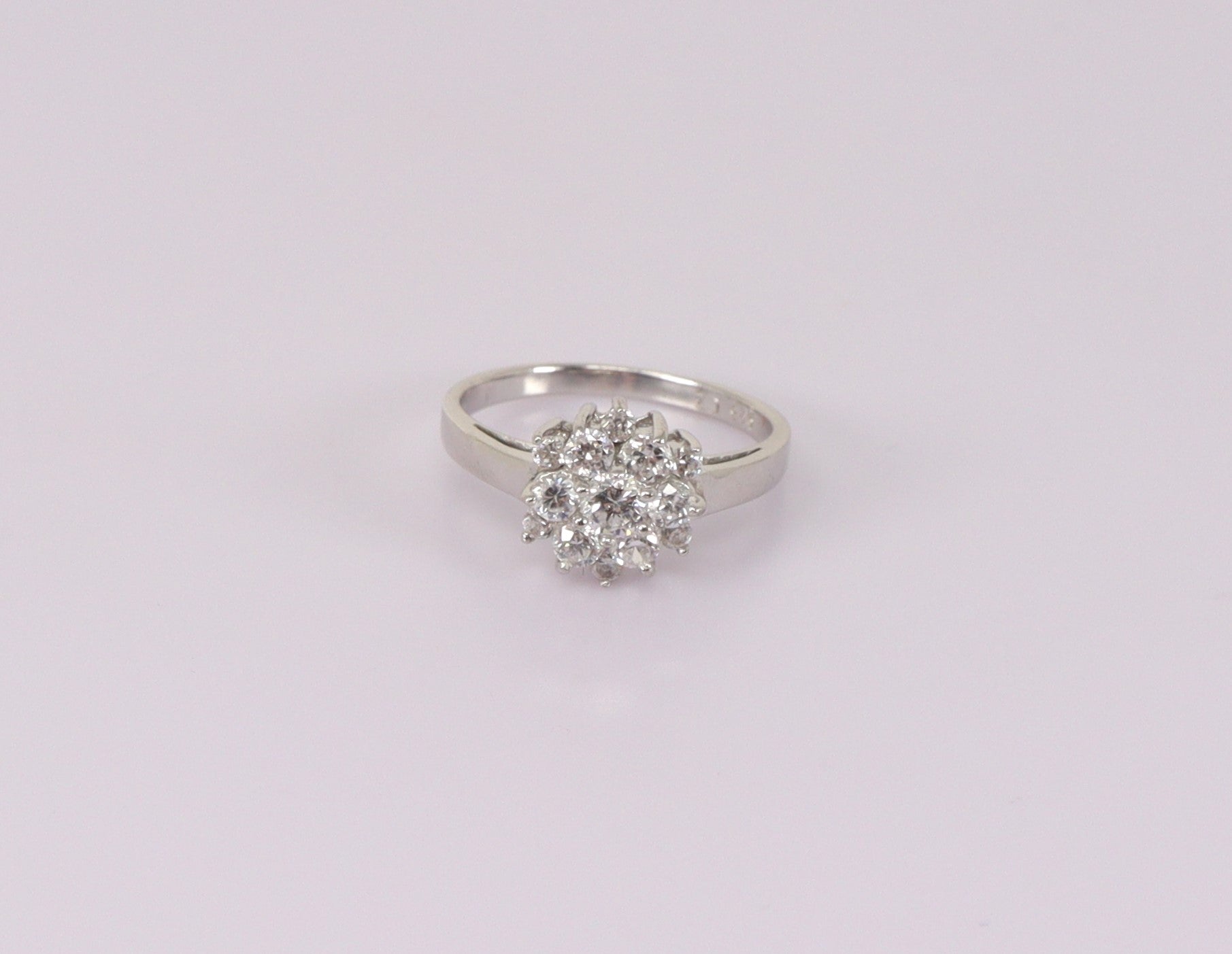 A silver cluster ring with cubic zirconia stones arranged in a daisy pattern, displayed against a white background.