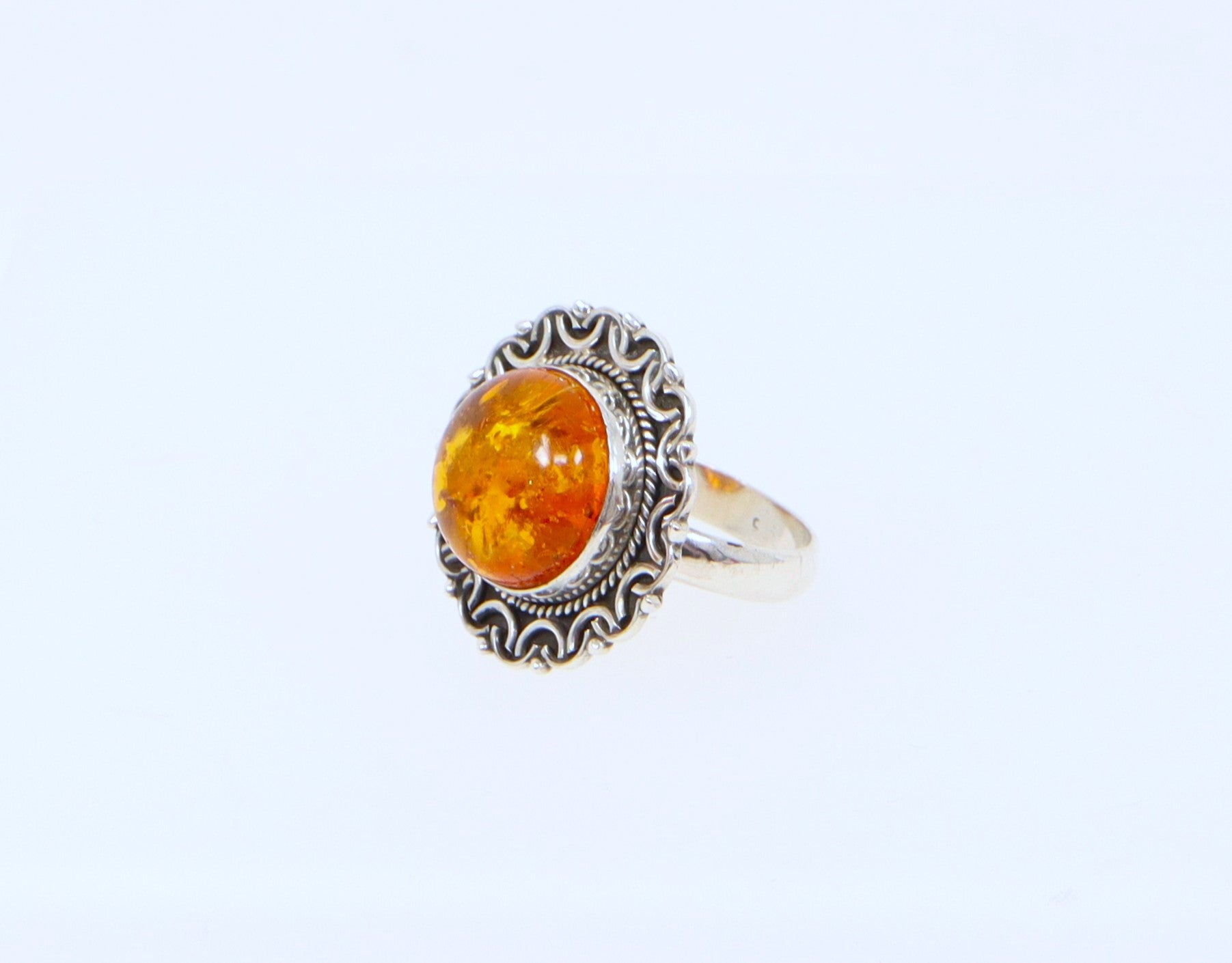 A ring with a round amber stone set in a sterling silver handcrafted setting with decorative elements.