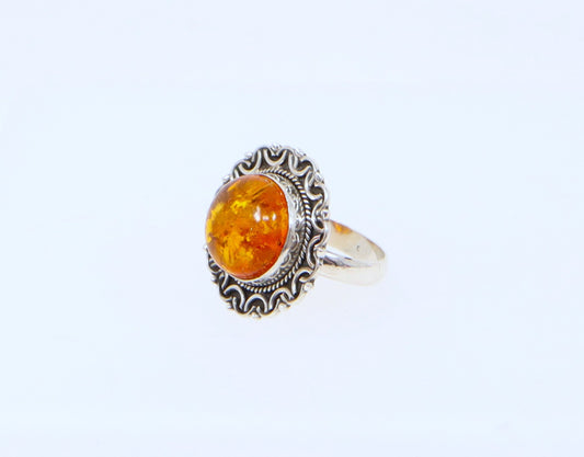 A ring with a round amber stone set in a sterling silver handcrafted setting with decorative elements.