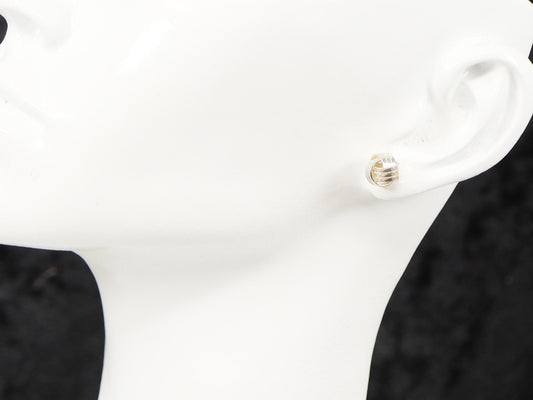 A pair of silver stud earrings with a knot design displayed on a mannequin ear.