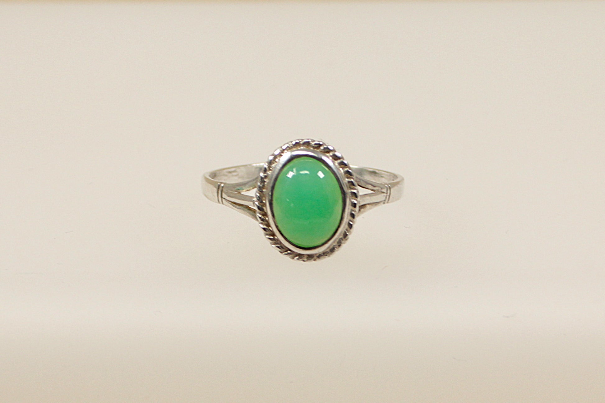 An oval cabochon chrysoprase gemstone set in a sterling silver ring with hallmarks visible inside the band.