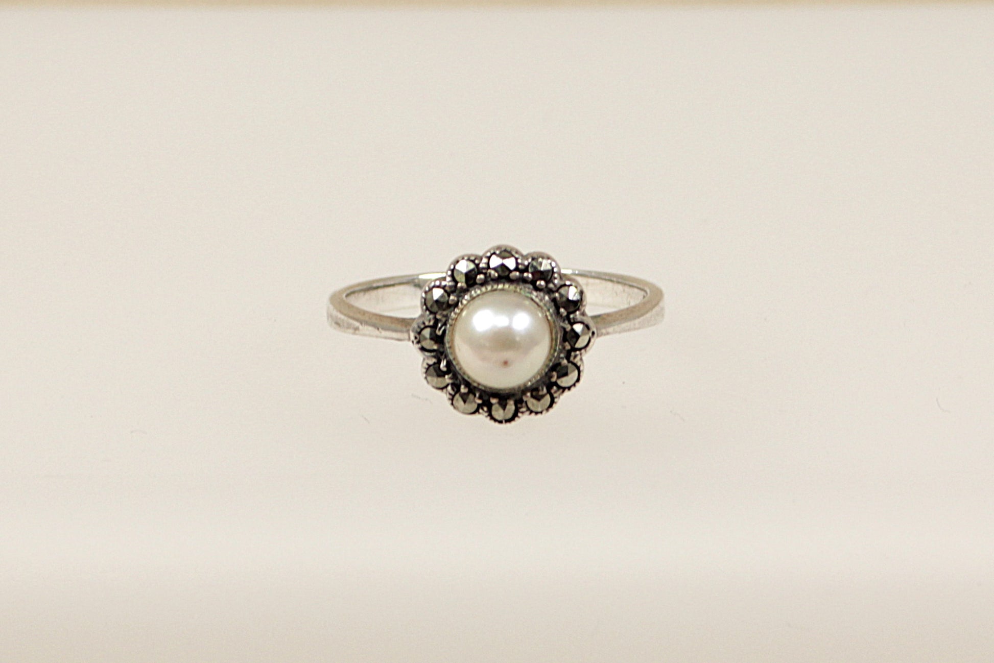 A silver ring with a central faux pearl surrounded by marcasite stones set in a circular pattern.