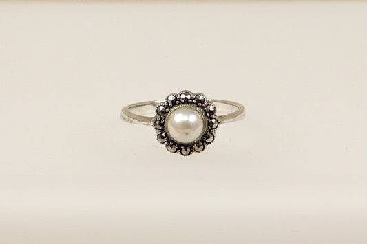 A silver ring with a central faux pearl surrounded by marcasite stones set in a circular pattern.