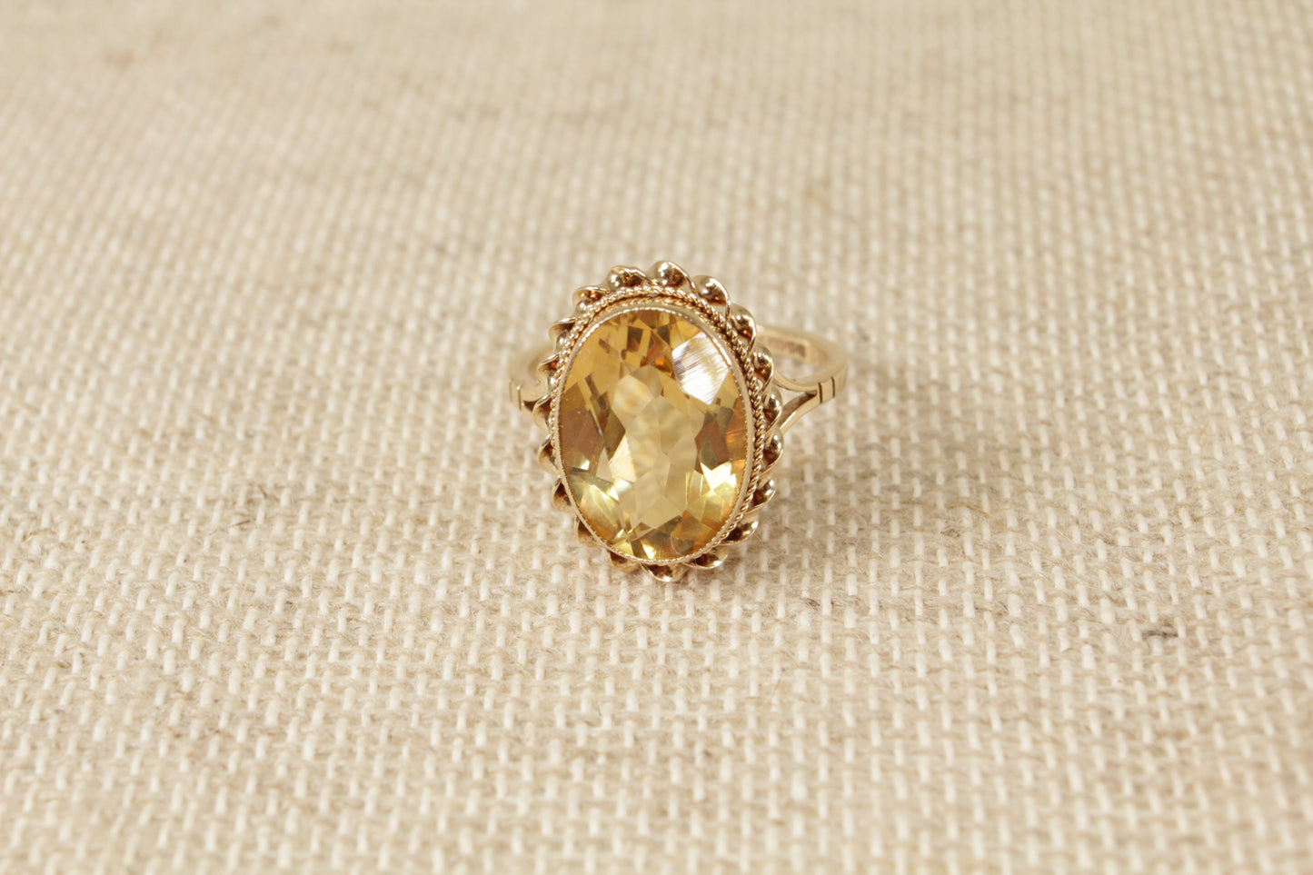 A vintage 9ct gold solitaire ring with an oval honey citrine gemstone, displayed against a textured background.