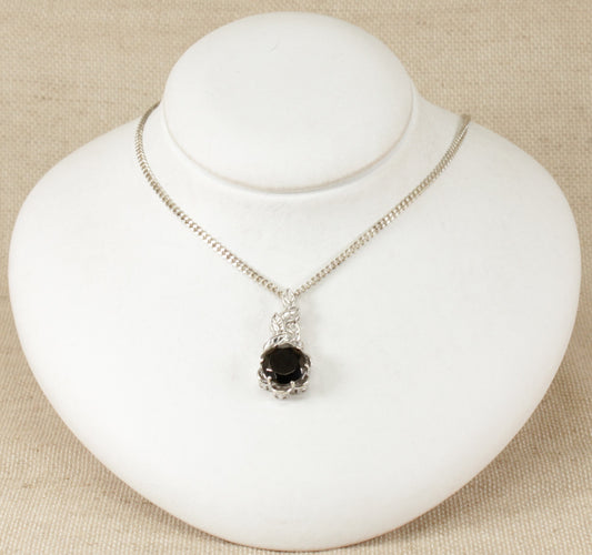 A silver pendant necklace with a round faceted crystal set in a leaf design setting, displayed on a white mannequin.