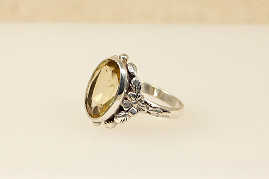 A vintage silver ring with a large oval citrine stone in an Art Nouveau style setting, featuring floral designs.