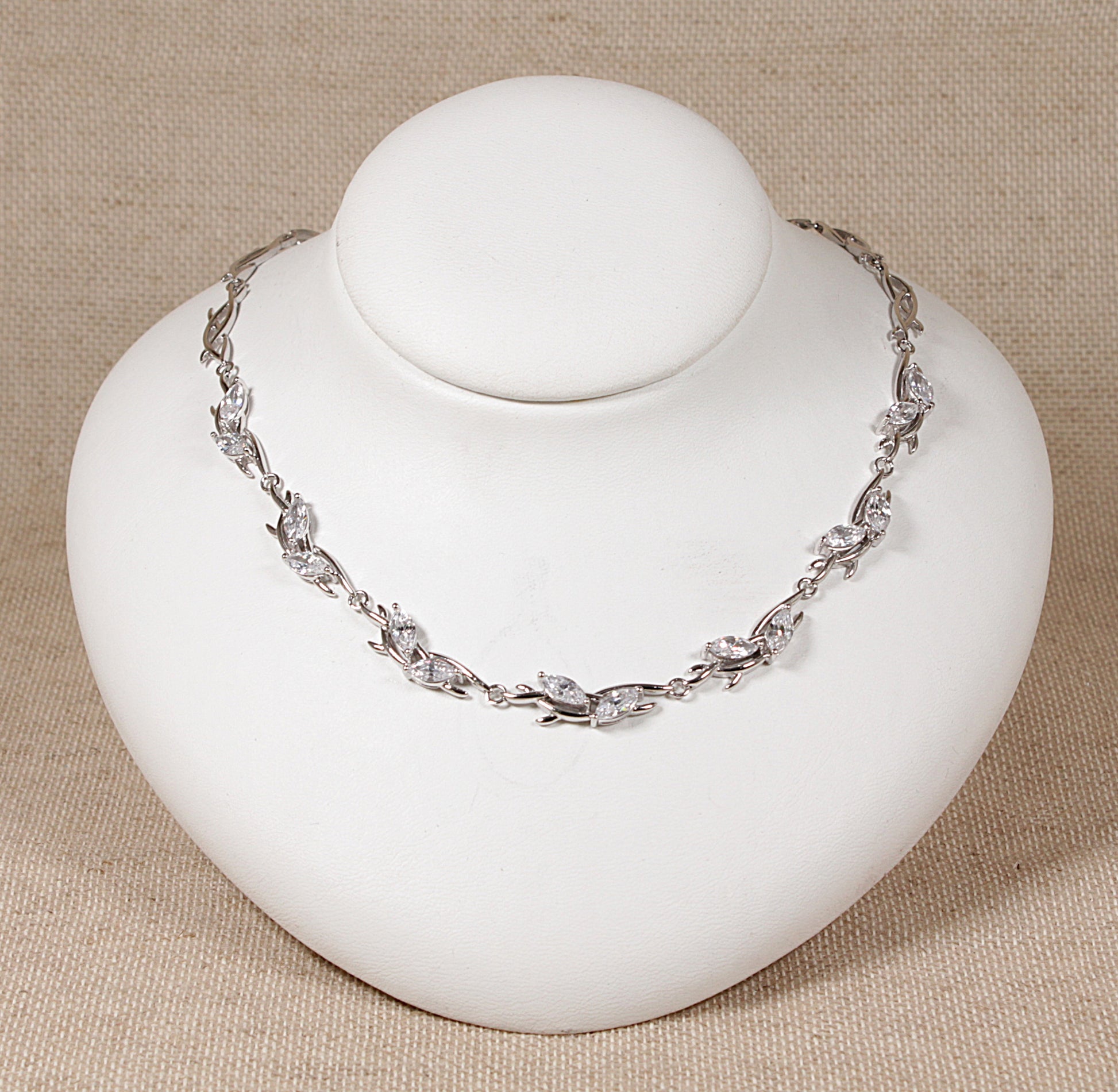 A silver necklace with cubic zirconia gemstones displayed on a white mannequin.