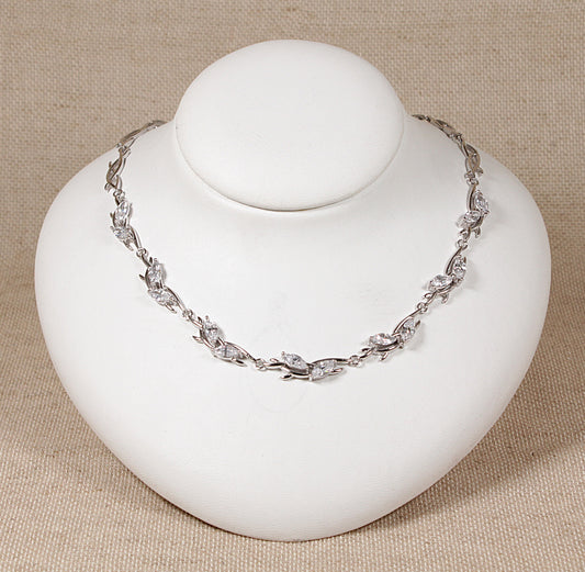 A silver necklace with cubic zirconia gemstones displayed on a white mannequin.