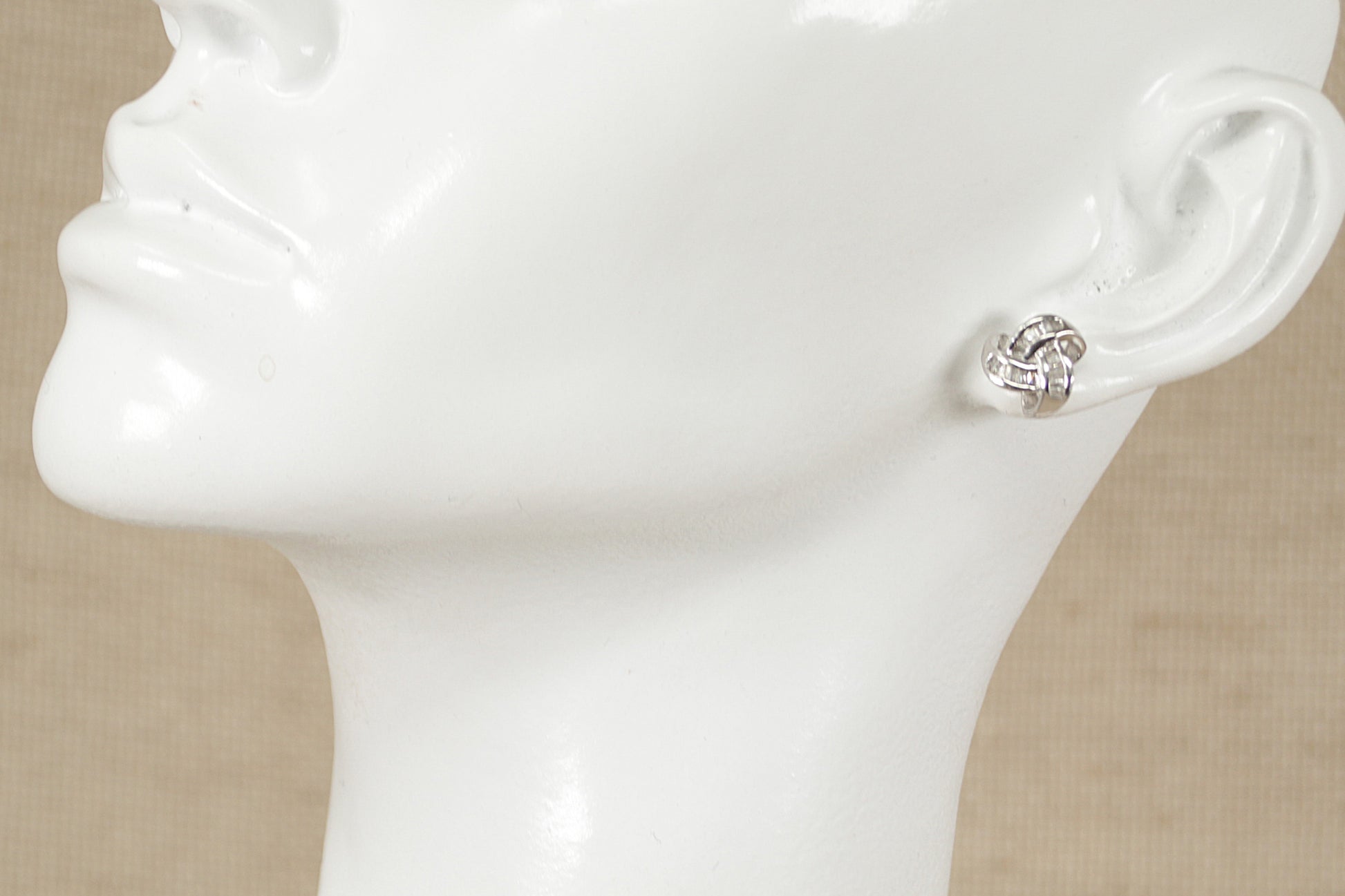 A pair of silver and cubic zirconia knot design stud earrings displayed on a mannequin head.