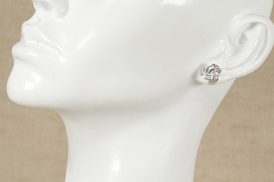 A pair of silver and cubic zirconia knot design stud earrings displayed on a mannequin head.
