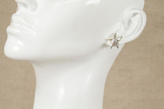 A pair of sterling silver starfish stud earrings displayed on a mannequin ear.