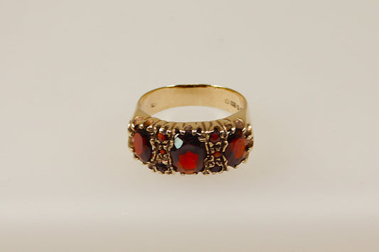 A vintage 9ct gold garnet ring with a classic design, featuring detailed filigree and milgrain patterns, and three prominent red garnets.