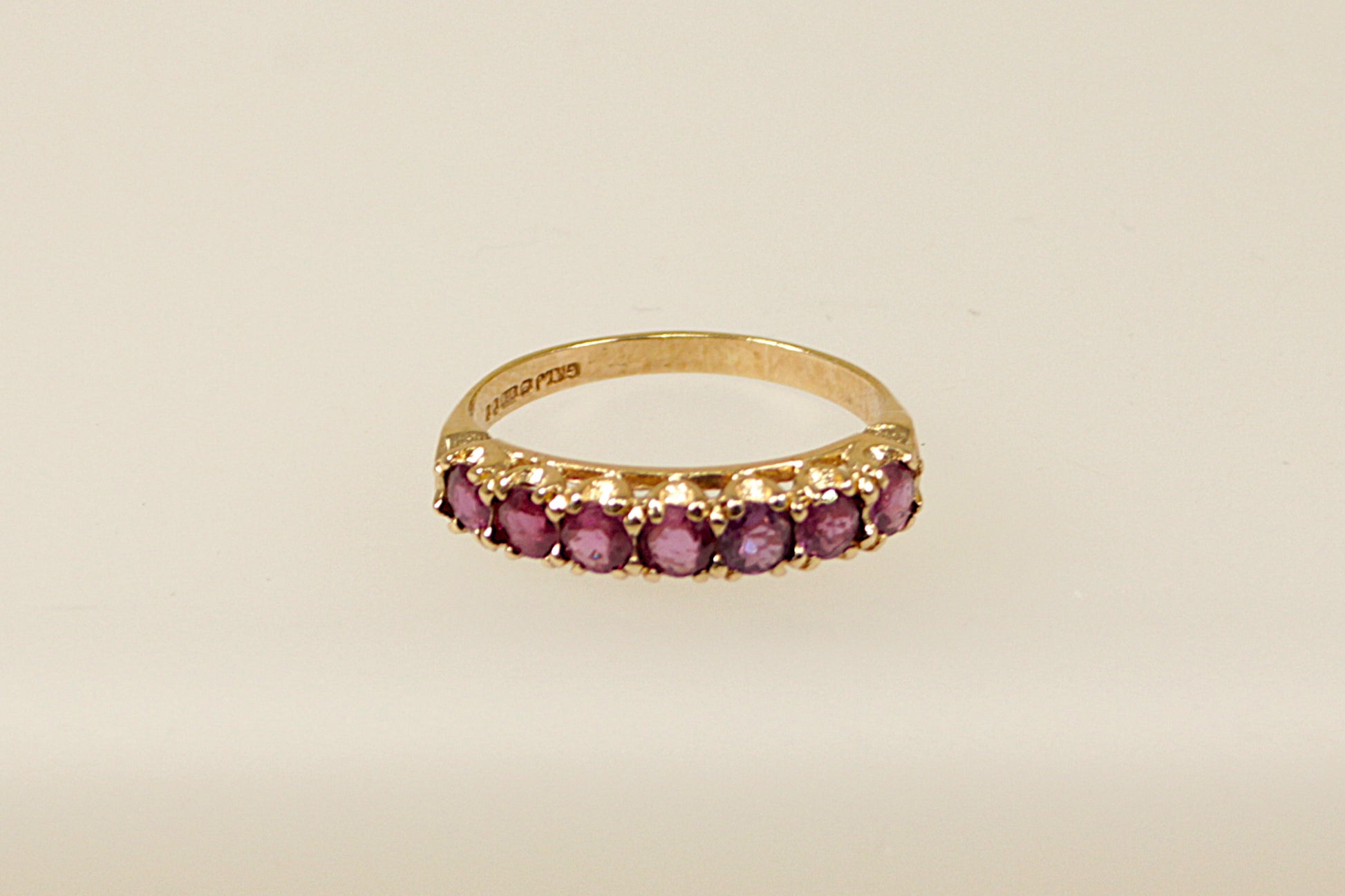 A vintage 9ct gold half eternity ring with seven claw set pink topaz gemstones on a white background.