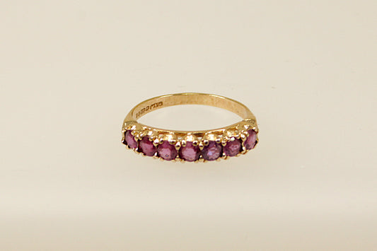 A vintage 9ct gold half eternity ring with seven claw set pink topaz gemstones on a white background.