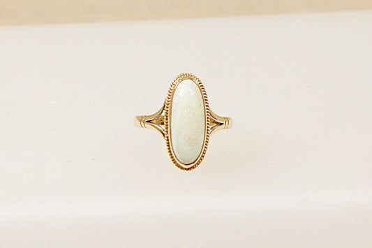 A 9ct gold ring with an oblong opal centered on a white background, showcasing the raised design and the band's elegance.
