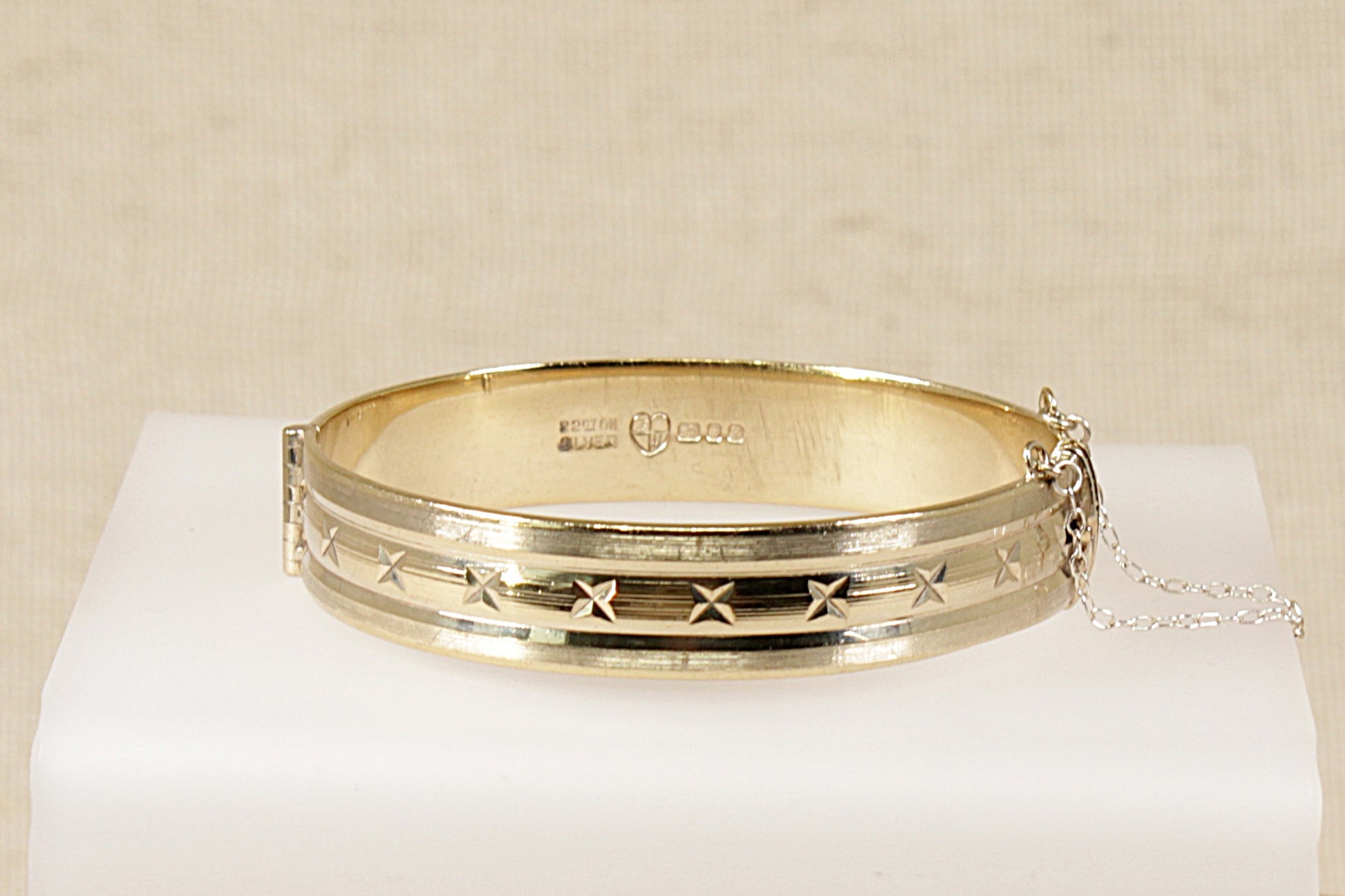 A vintage solid silver bangle bracelet with a geometric design, plated with 22ct gold, displayed on a white surface.
