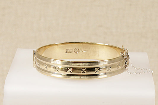 A vintage solid silver bangle bracelet with a geometric design, plated with 22ct gold, displayed on a white surface.