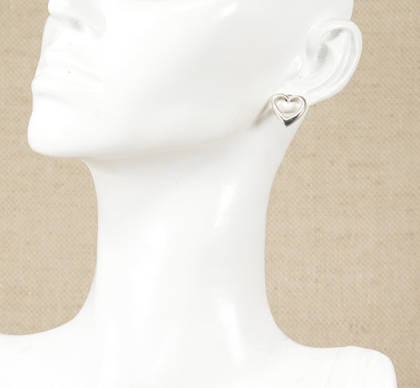 A pair of silver heart-shaped stud earrings displayed on a mannequin head.