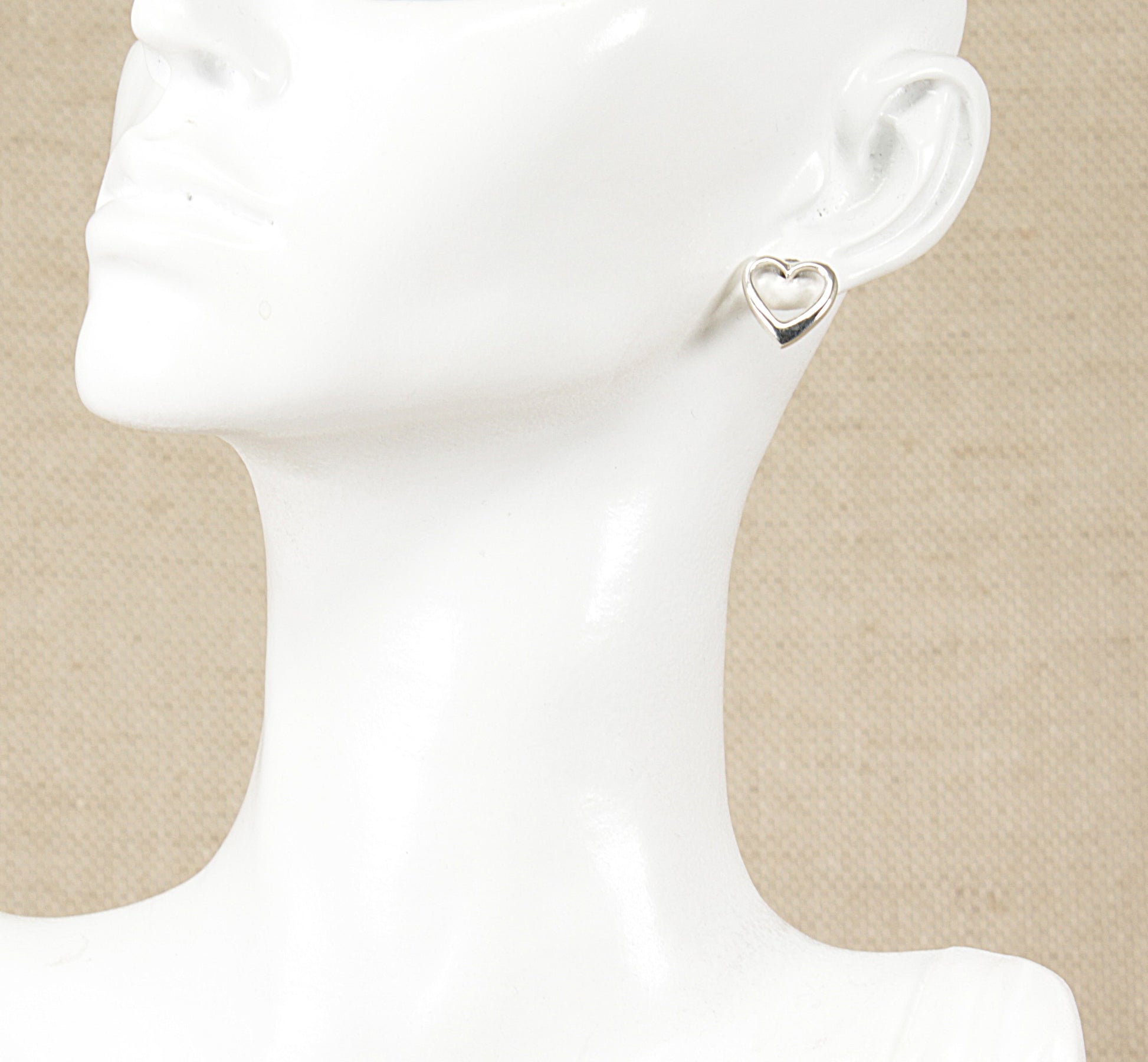 A pair of silver heart-shaped stud earrings displayed on a mannequin head.