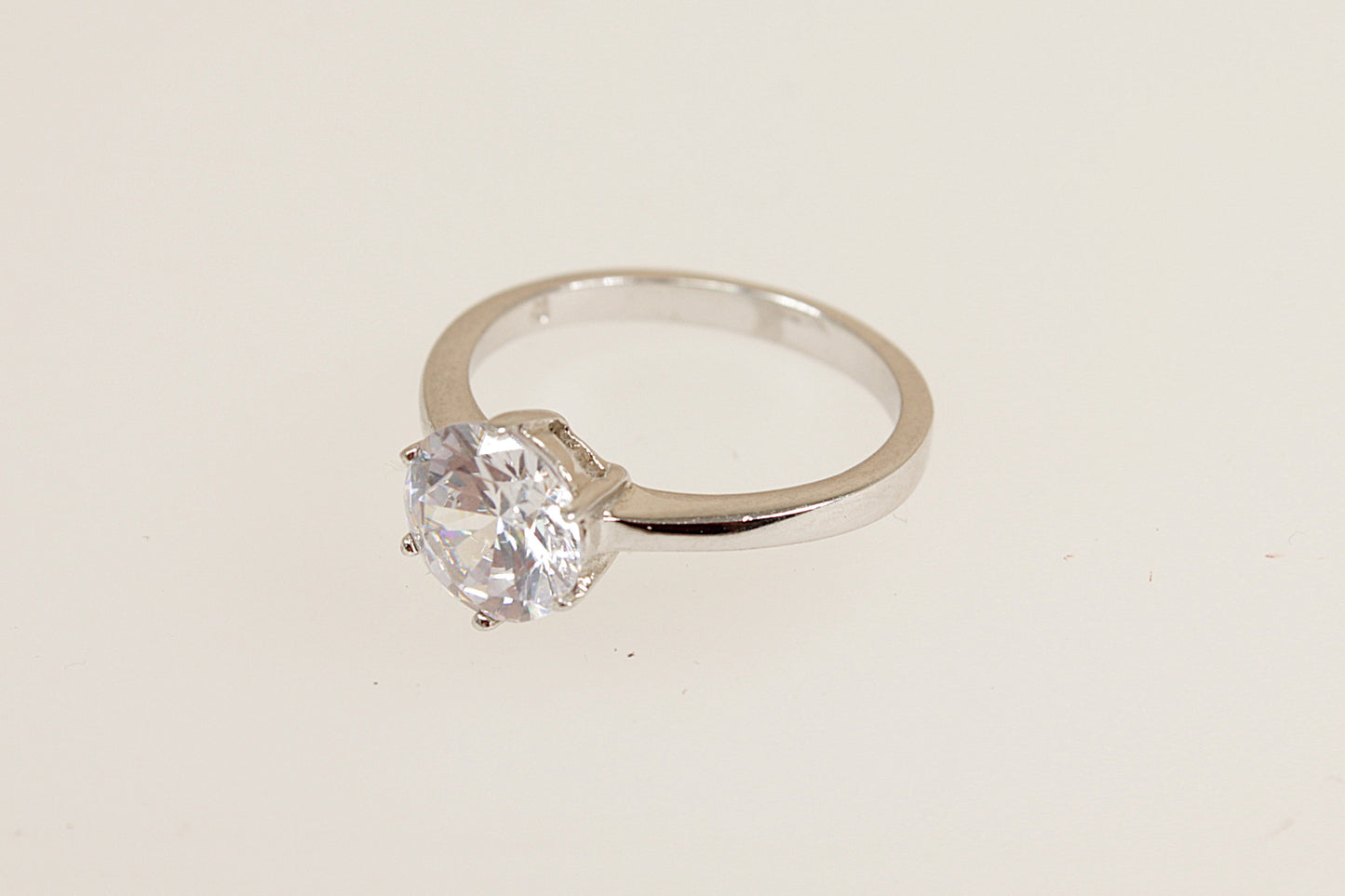 Silver solitaire ring with a clear gemstone on a beige background