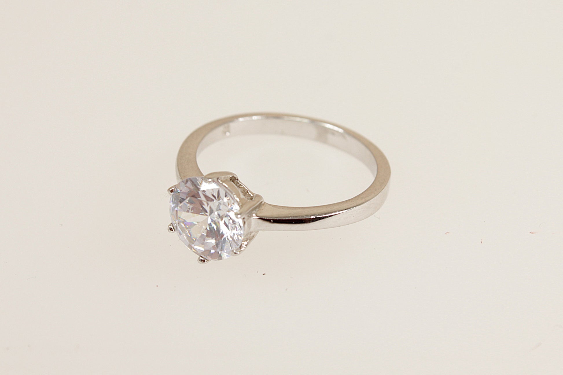 Silver solitaire ring with a clear gemstone on a beige background
