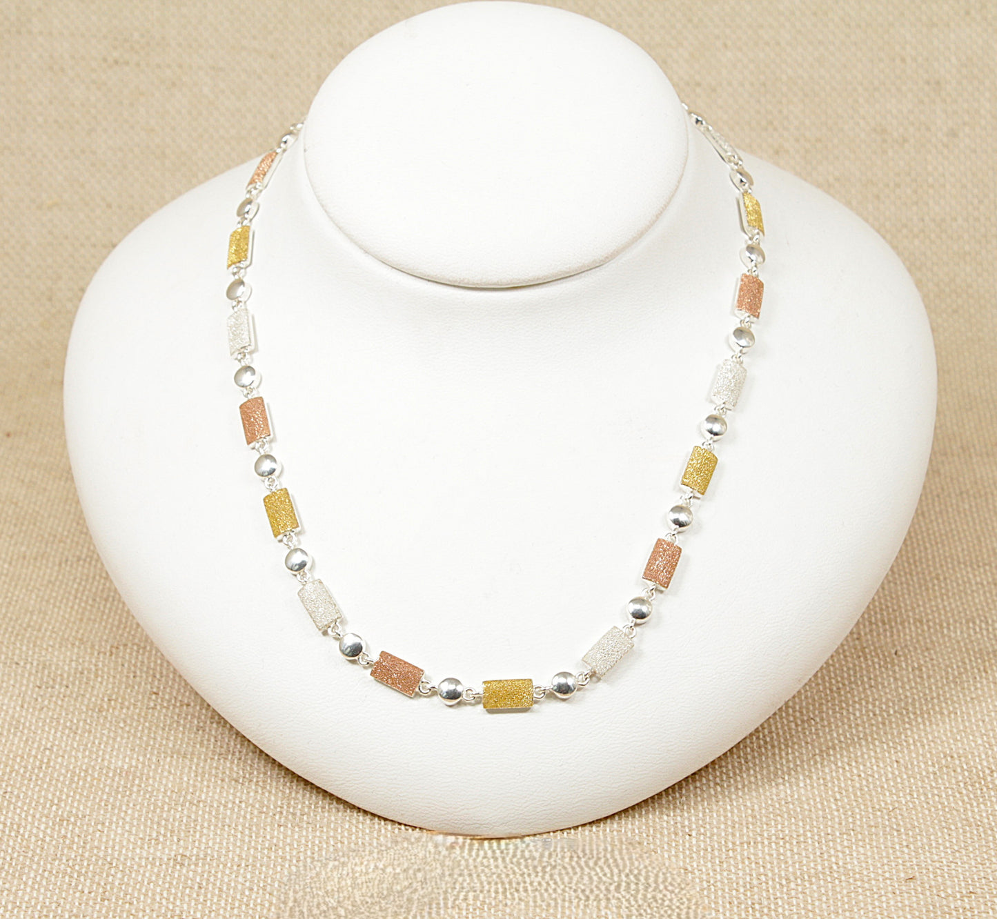 A silver necklace with tri colour beads displayed on a white mannequin.