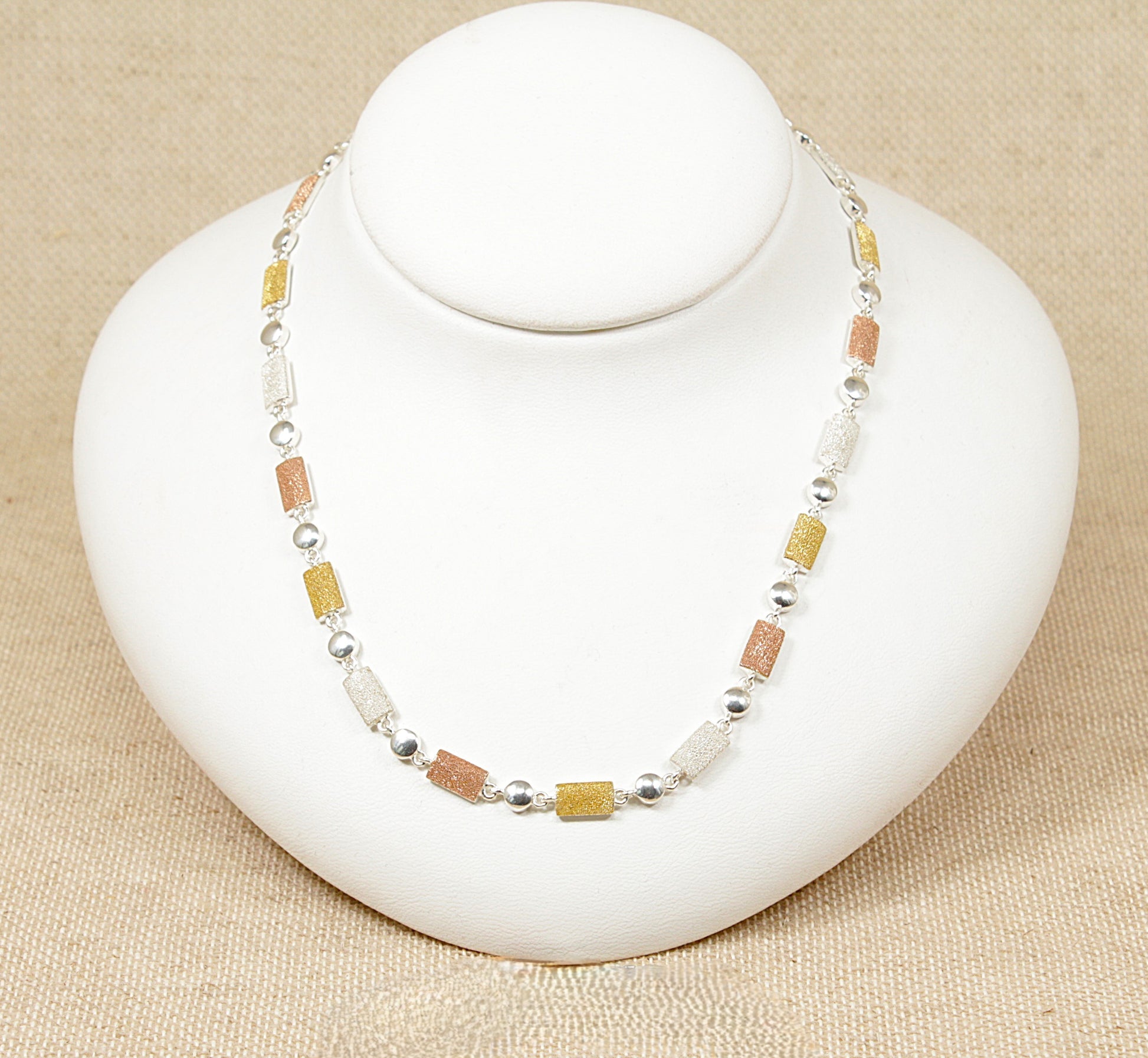 A silver necklace with tri colour beads displayed on a white mannequin.