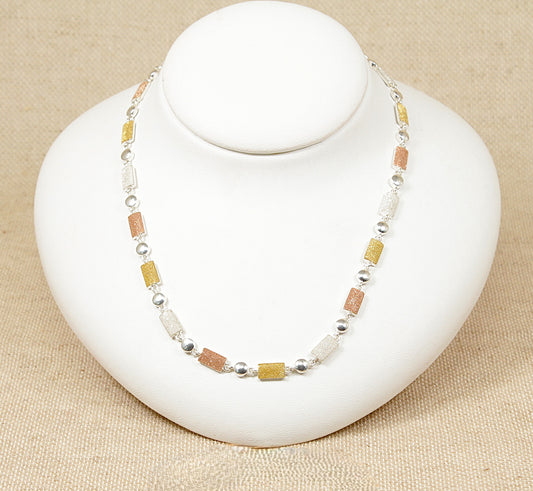 A silver necklace with tri colour beads displayed on a white mannequin.
