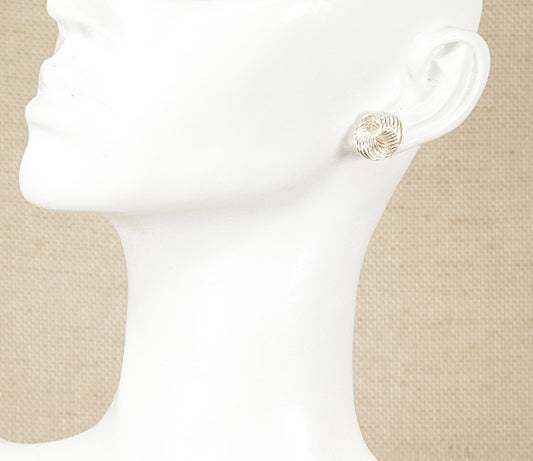 A pair of silver stud earrings with a round, swirling pattern displayed on a mannequin ear.