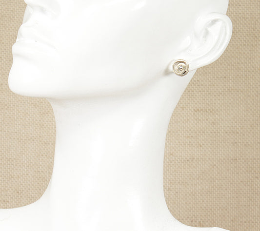 A pair of silver stud earrings with a cubic zirconia gemstone displayed on a mannequin ear.