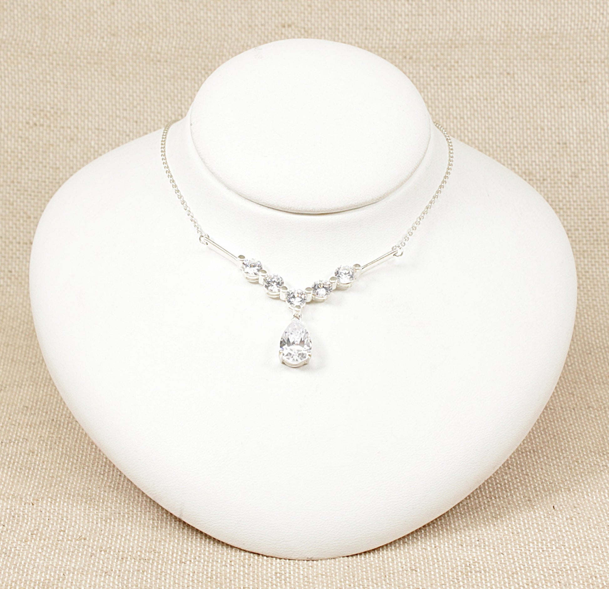 This silver necklet features an elegant arrangement of cubic zirconia gemstones, creating a sparkling and sophisticated look. The design includes five round CZ stones set along a V-shaped mount, which adds a graceful contour to the necklace. The V shape not only accentuates the neckline but also gives a modern and refined touch to the piece. The necklet is in excellent condition and stamped 925 for sterling silver.