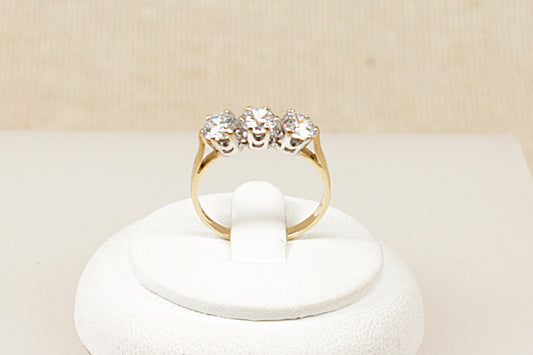 Gold ring with three cubic zirconia gemstones on a white stand against a beige background
