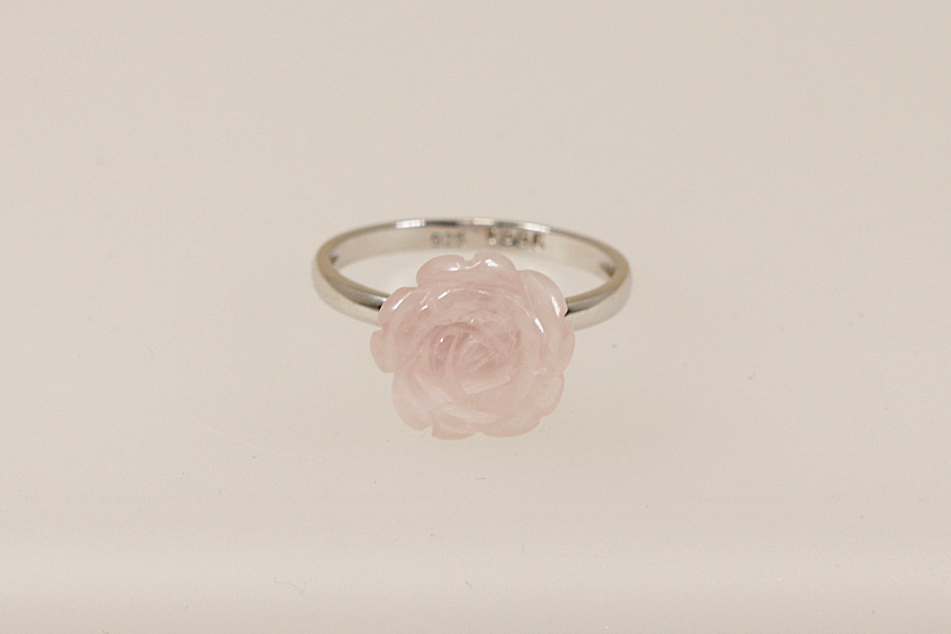 A silver ring with a carved pink rose as the central stone, displayed against a white background.