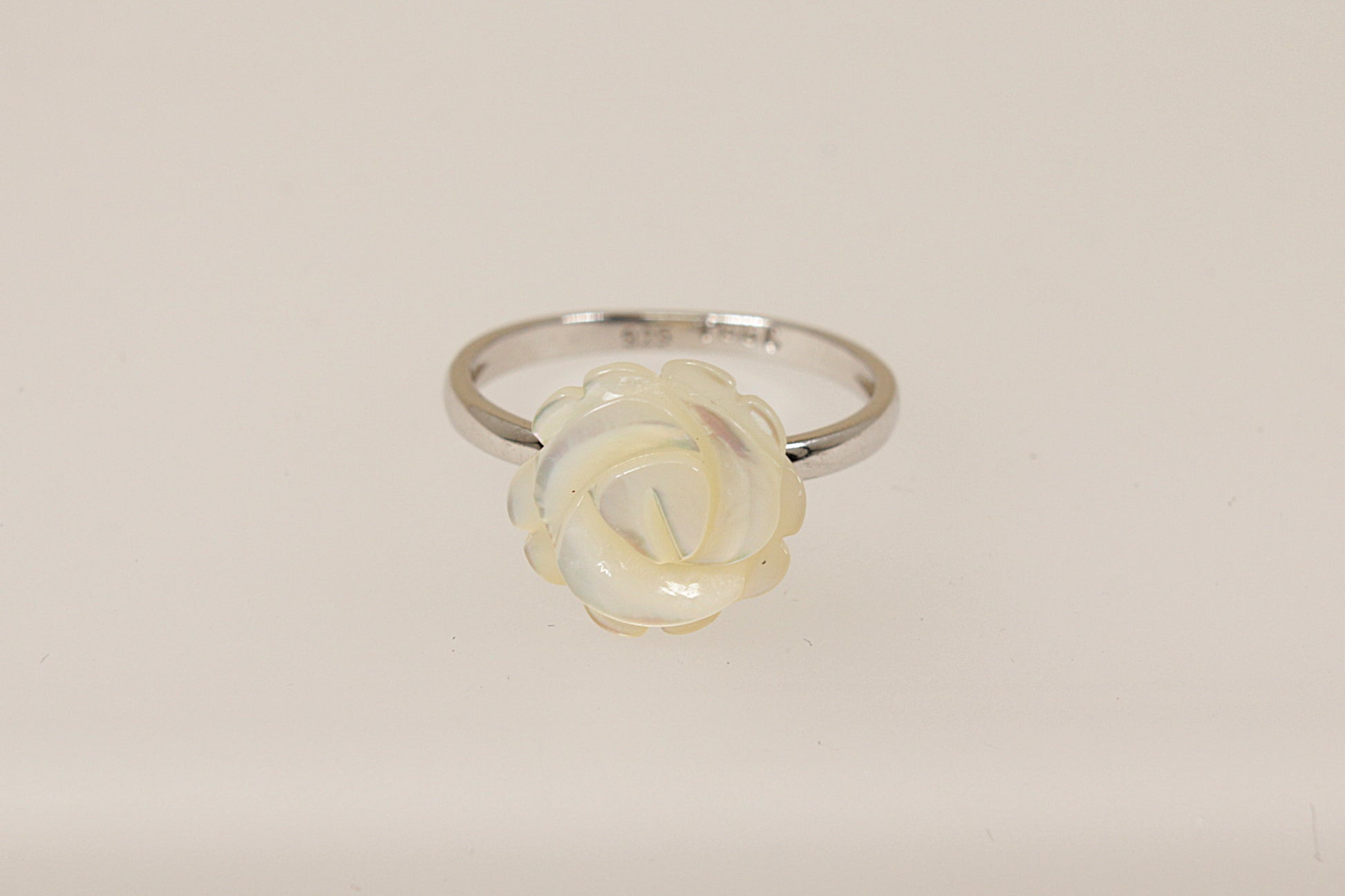 A silver ring with a carved white mother of pearl rose in full bloom on a white background.