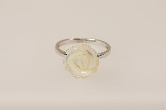 A silver ring with a carved white mother of pearl rose in full bloom on a white background.