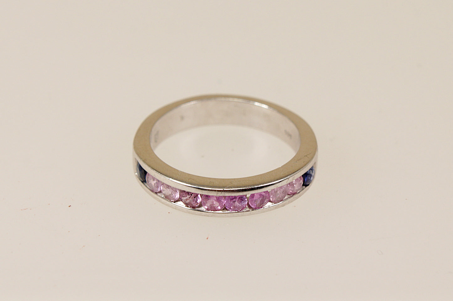 A sterling silver half eternity ring with a series of round-cut pink topaz gemstones channel-set within the band, with two deep blue sapphire stones at each end.