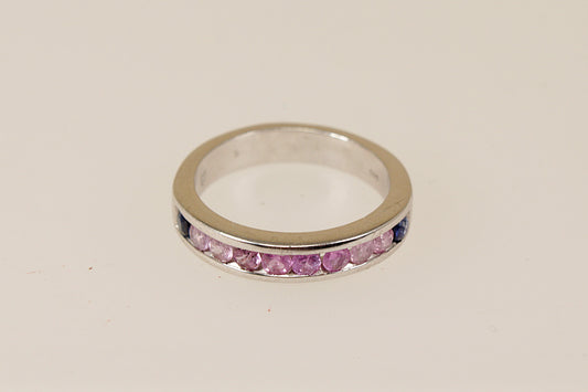 A sterling silver half eternity ring with a series of round-cut pink topaz gemstones channel-set within the band, with two deep blue sapphire stones at each end.