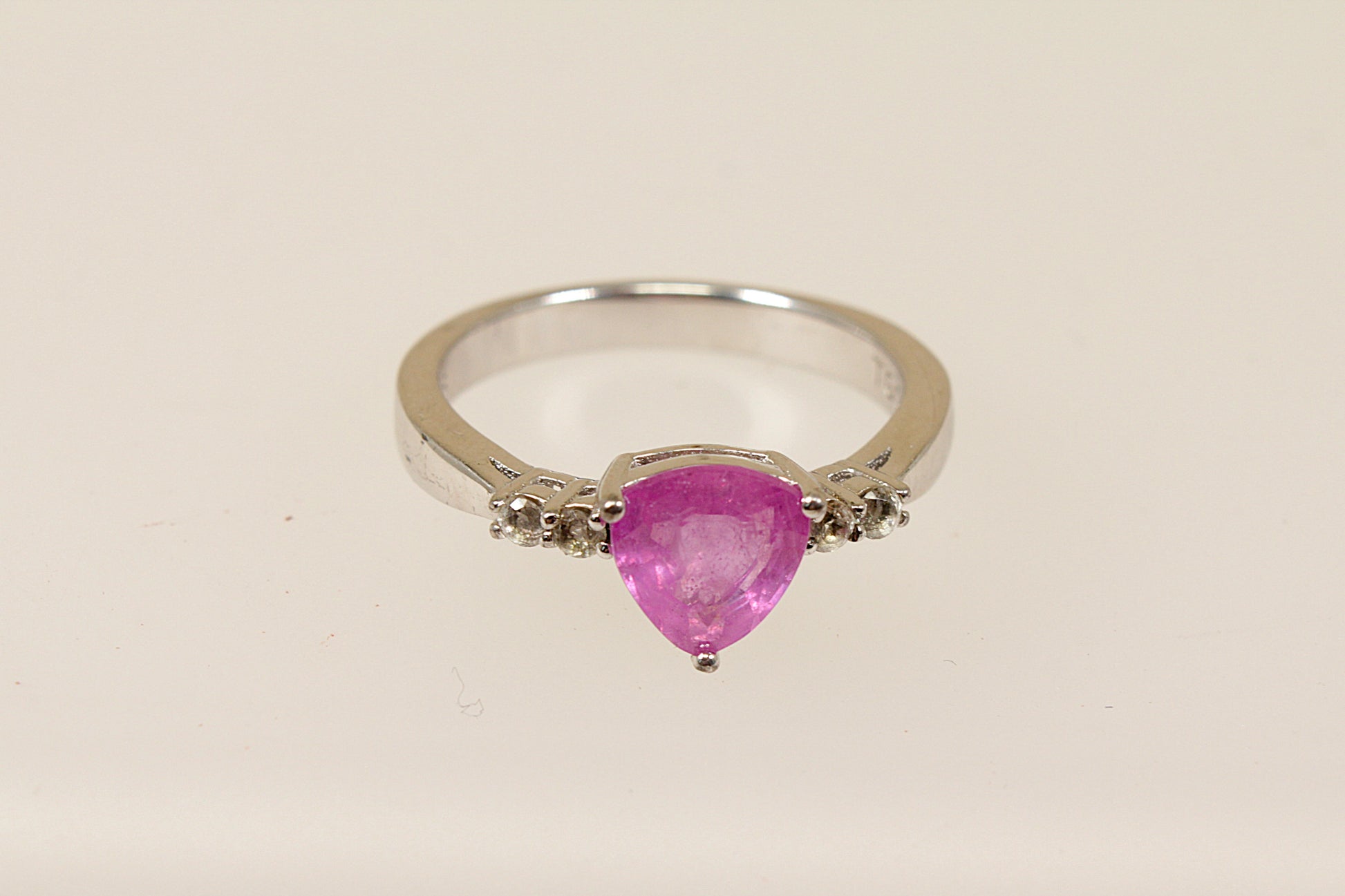 A sterling silver trillion cut pink sapphire solitaire ring with white topaz accents, Stamped 925 for sterling silver and the makers mark ‘TGGC’ for The Genuine Gemstone Company, UK  finger size O.