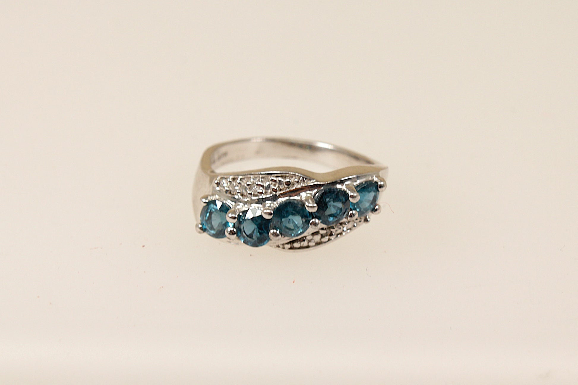 A sterling silver ring with five round blue topaz gemstones set across the band in a graceful curve with claw settings.